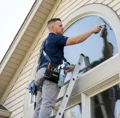 Professional window cleaner on a ladder using a squeegee to clean an exterior arched window, Dayton, OH.